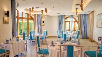 A dining area with tables and chairs, large windows, and a ceiling with recessed lighting.