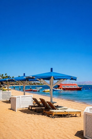 A beach with sun loungers, umbrellas, and a red boat in the water. - Safir Dahab Resort (Dahab)
