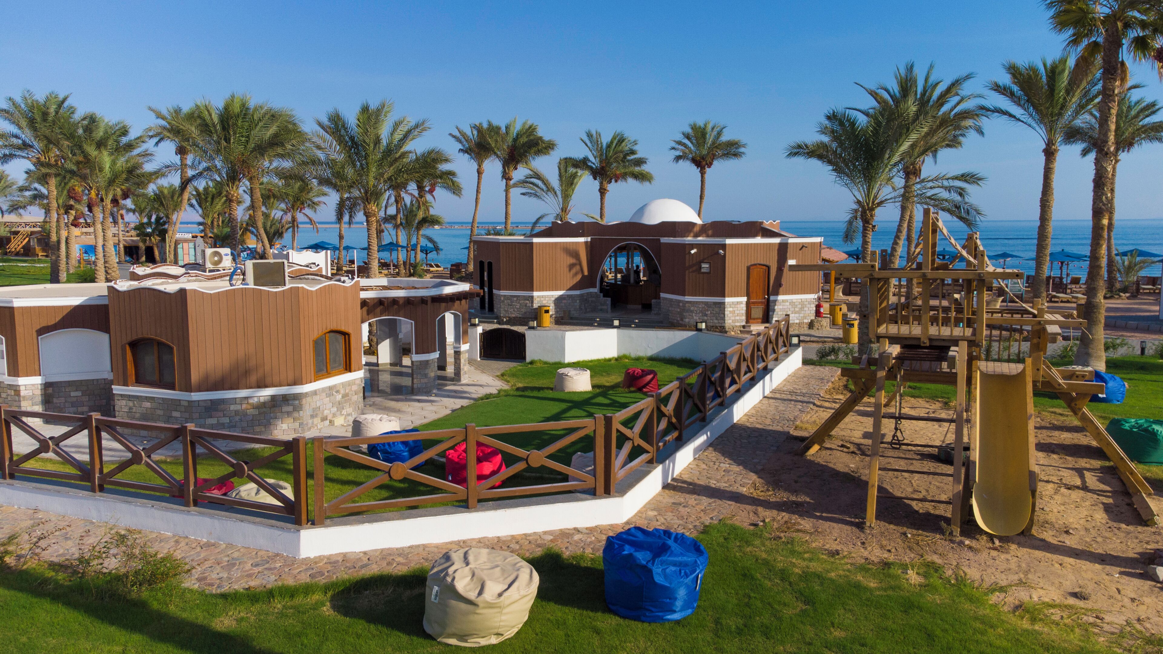 Een resort met een zwembad, palmbomen en uitzicht op het strand.