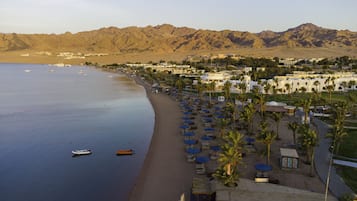 Enjoy a serene beachfront setting with a wide sandy beach, sun loungers, and umbrellas for relaxation, plus a marina with several boats.