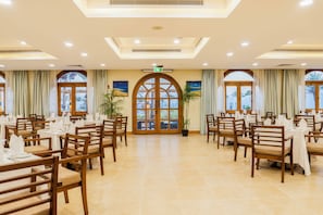 A restaurant with multiple tables and chairs, large windows with curtains, and a central door with an exit sign. - Safir Dahab Resort (Dahab)