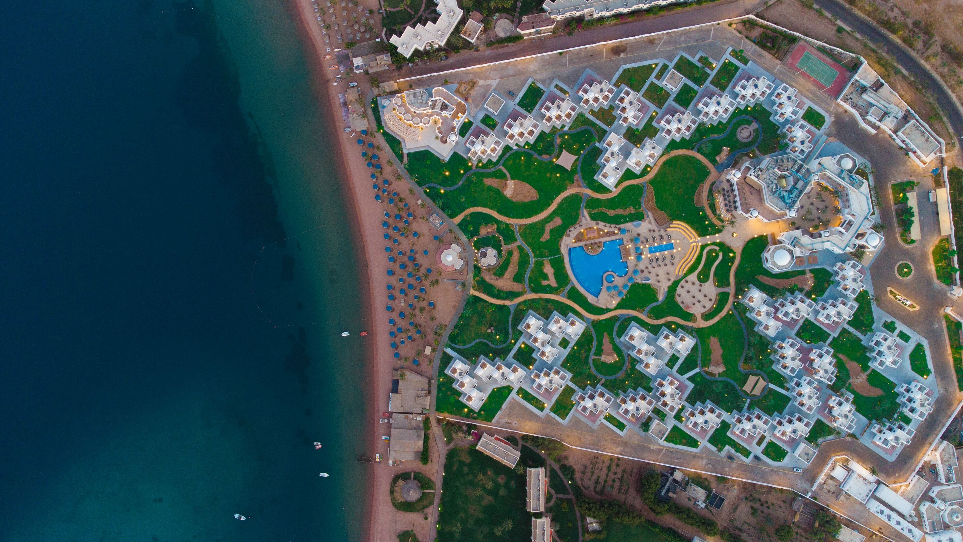 An aerial view of a resort with multiple buildings, a beach, and a swimming pool.