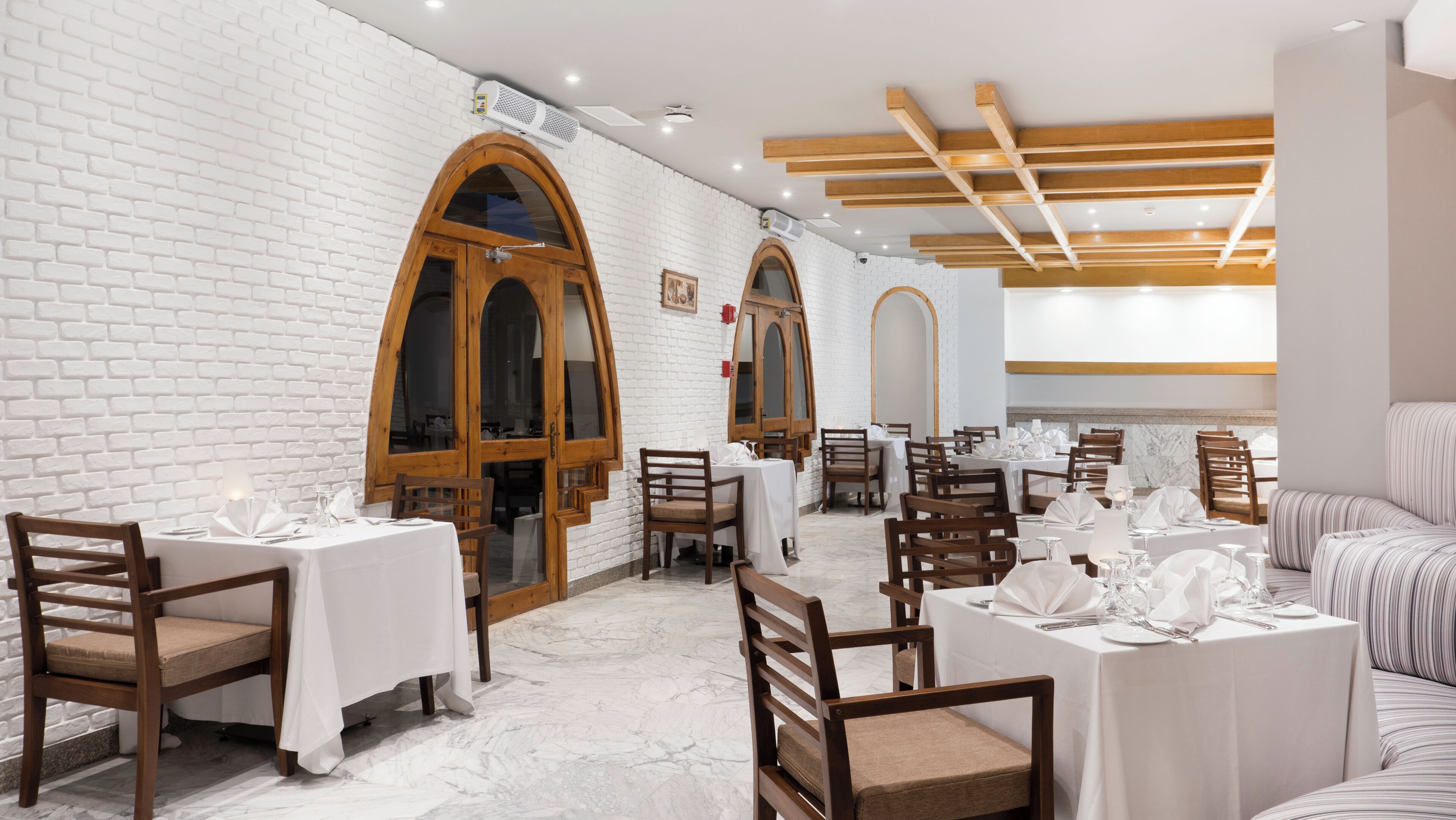 Un restaurante con paredes de ladrillo blanco, puertas de madera y mesas preparadas para comer.