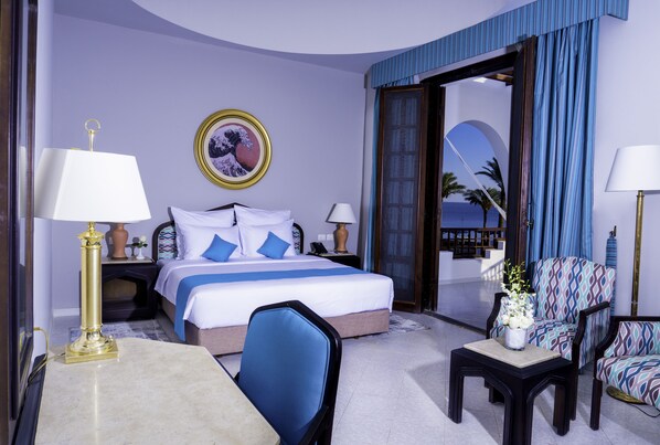 A hotel room with a bed, two chairs, a table, a nightstand, and a view of the sea. - Safir Dahab Resort (Dahab)
