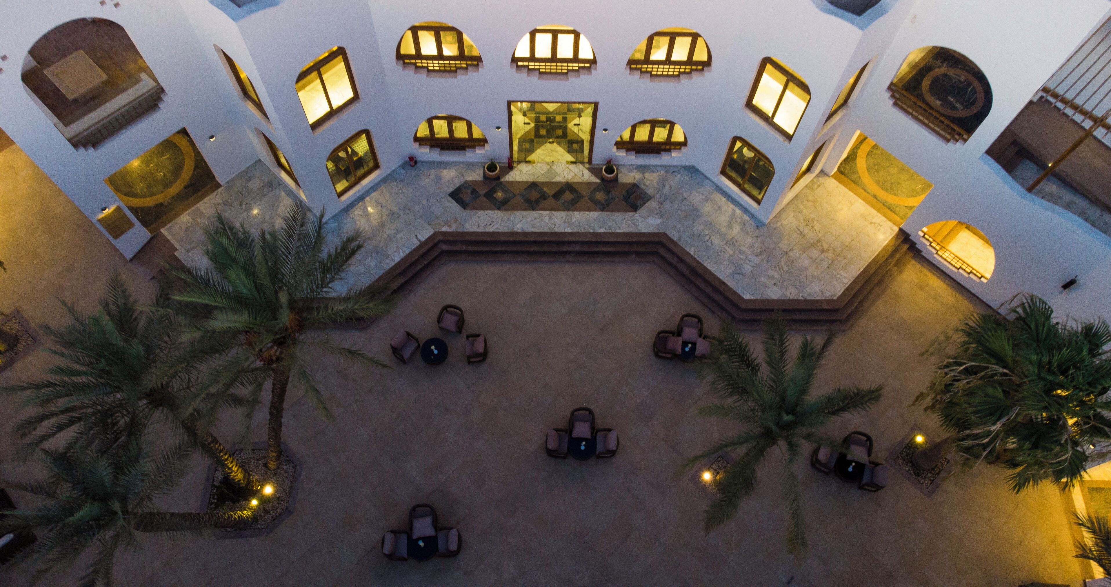 An aerial view of a hotel lobby with a central seating area, palm trees, and a patterned floor.