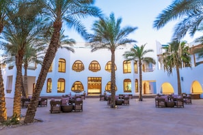 Un patio de hotel con palmeras, asientos al aire libre y un edificio con ventanas de arco.