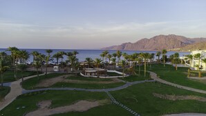 A resort with a pool area, palm trees, and a view of the sea and mountains. - Safir Dahab Resort (Dahab)