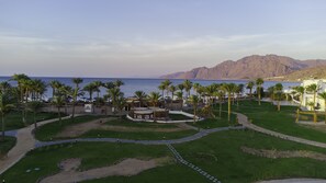 A resort with a pool area, palm trees, and a view of the sea and mountains. - Safir Dahab Resort (Dahab)