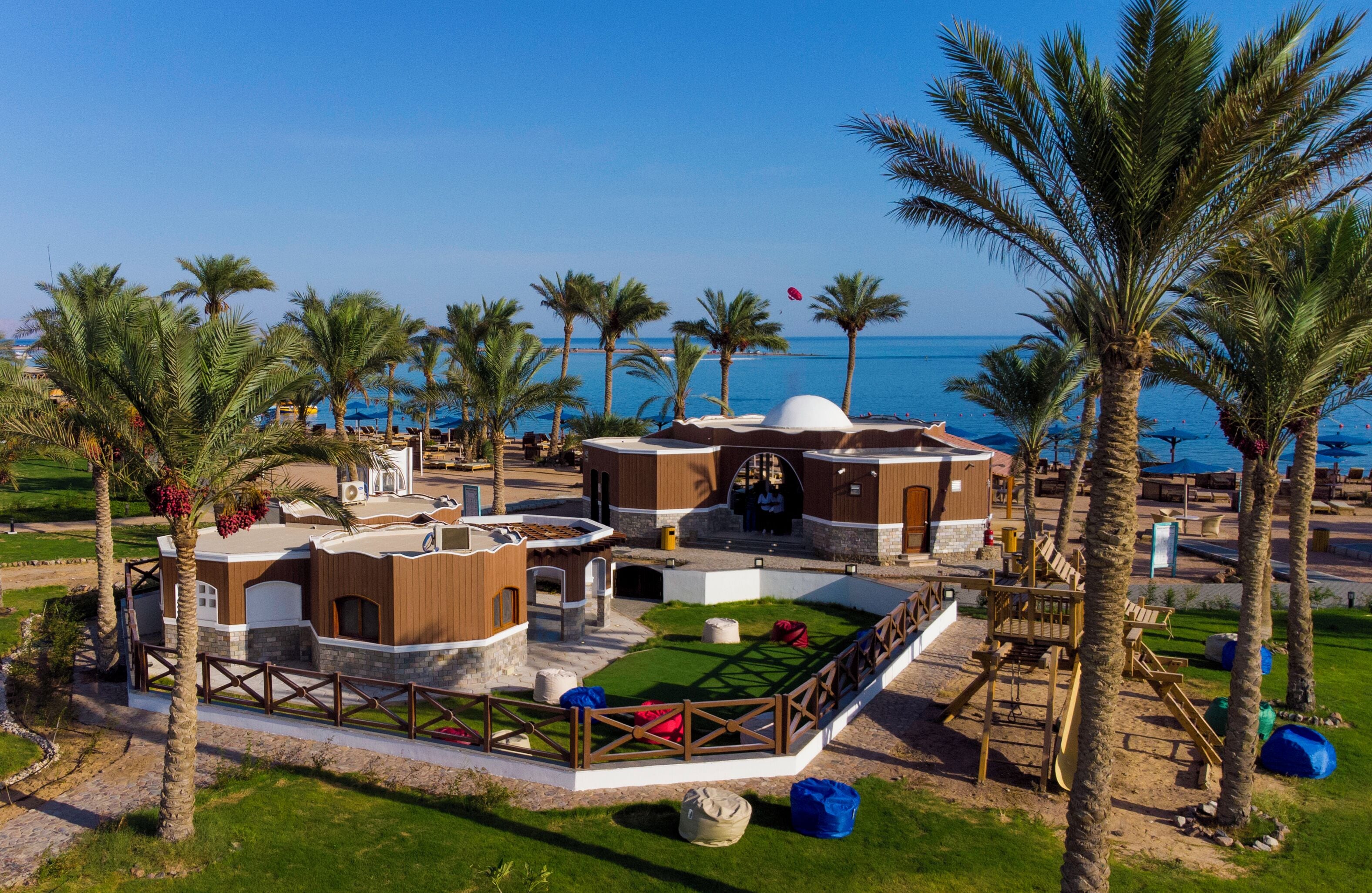 A resort with multiple buildings, palm trees, and a view of the sea.