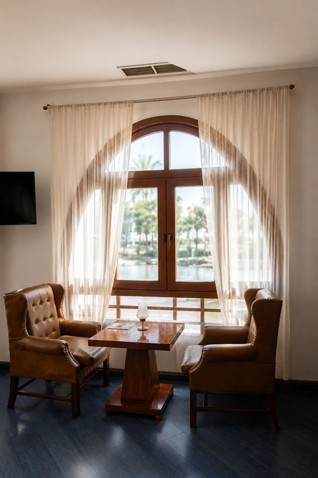 Una habitación con un amplio ventanal de arco, dos sillones de cuero, una mesa de centro de madera y un televisor de pantalla plana montado en la pared.