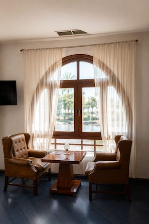Una habitación con un amplio ventanal de arco, dos sillones de cuero, una mesa de centro de madera y un televisor de pantalla plana montado en la pared.