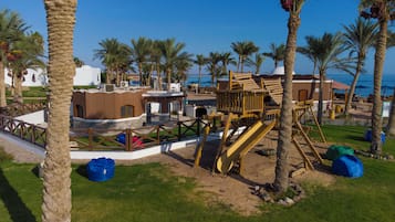 A resort with palm trees, a wooden play structure, and a beach view.