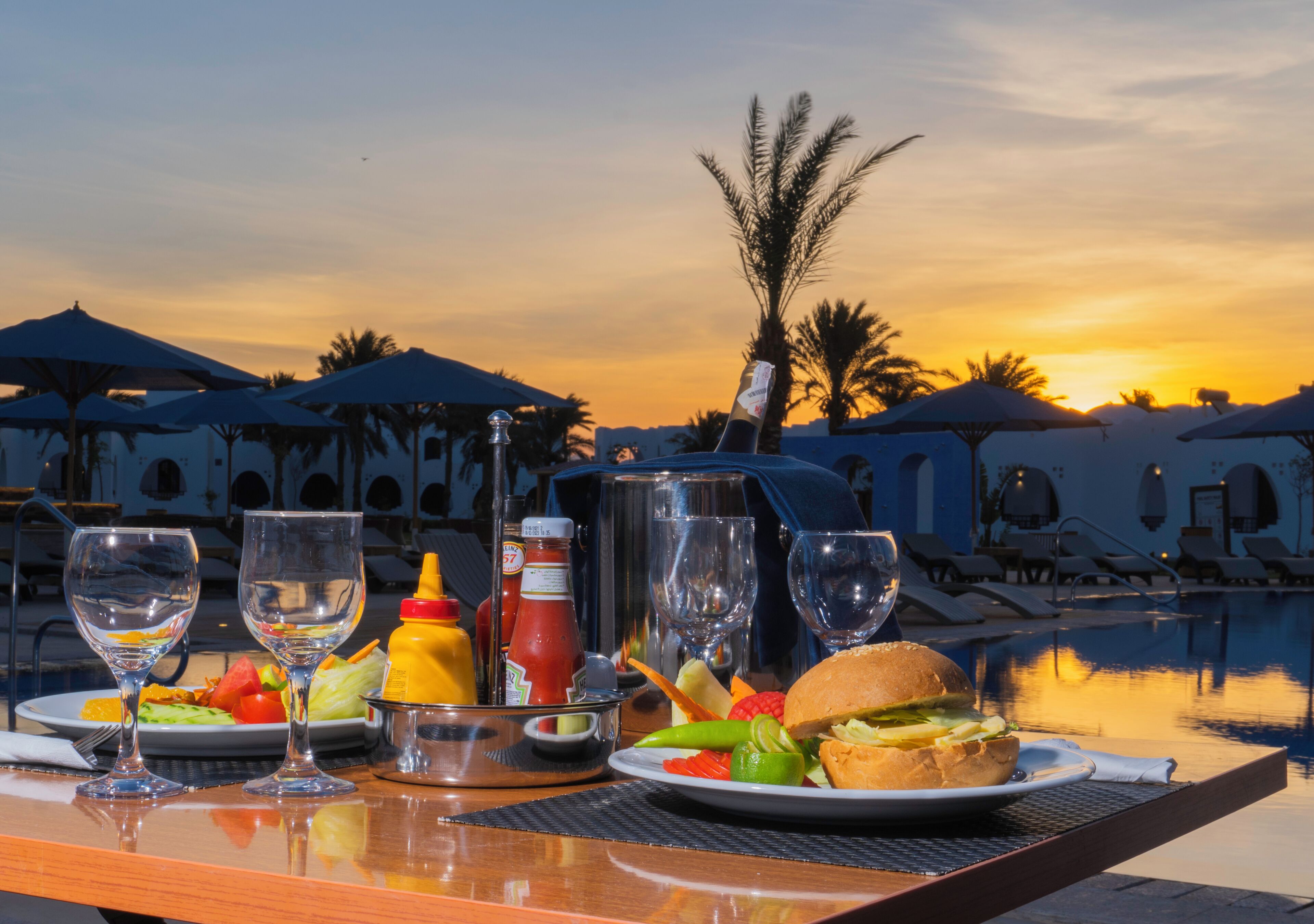 Mesa lista para una comida con vista a la puesta de sol sobre una zona de piscina.