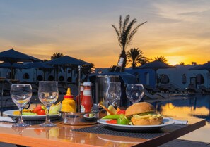 Ein Tisch ist für eine Mahlzeit gedeckt, mit Blick auf einen Pool bei Sonnenuntergang.
