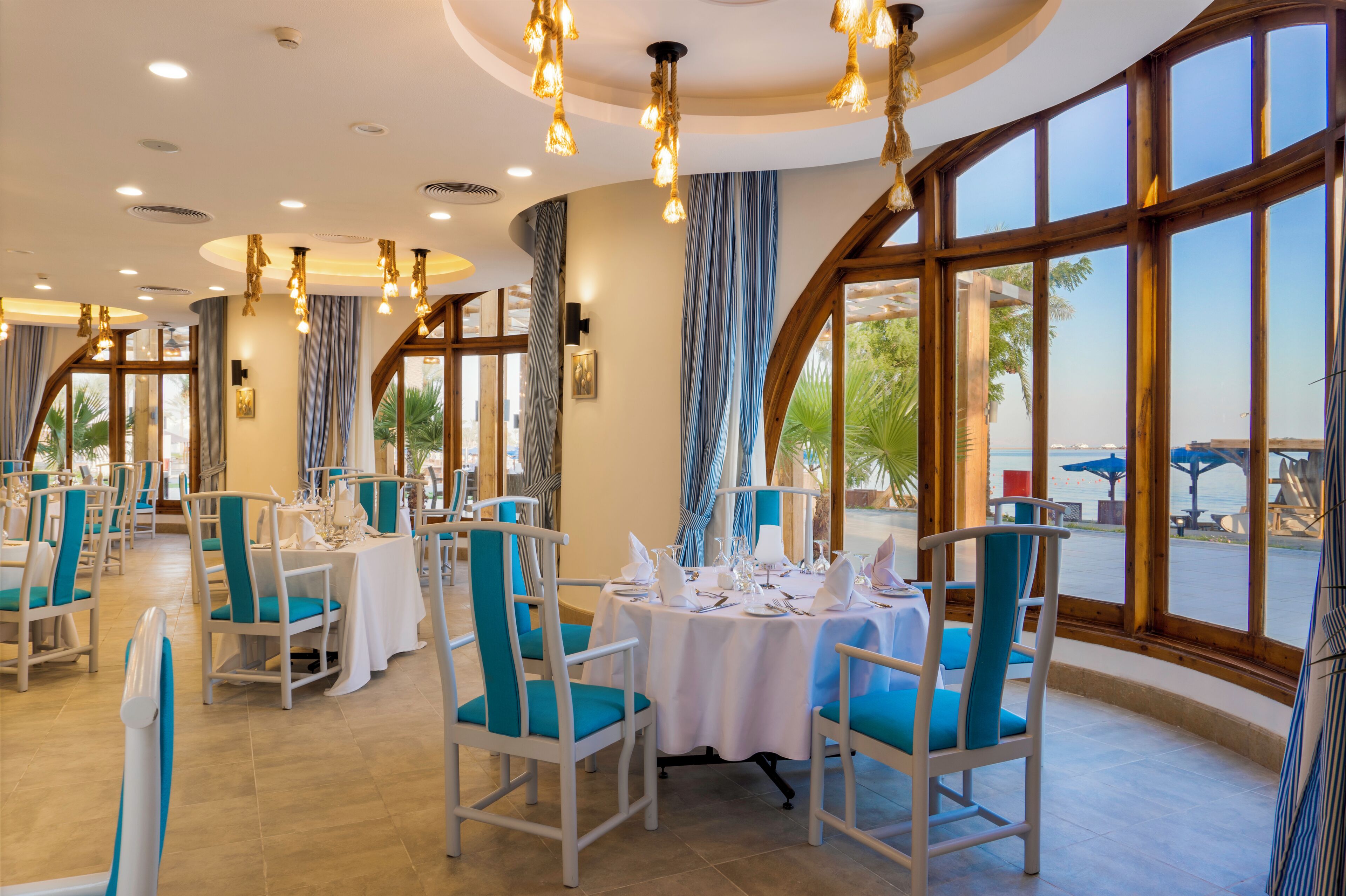 Ein Restaurant mit runden Tischen, blauem Stuhl und großen Fenstern mit Blick ins Freie.