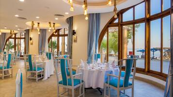 Ein Restaurant mit runden Tischen, blauem Stuhl und großen Fenstern mit Blick ins Freie.
