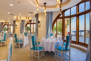 Un restaurante con mesas redondas dispuestas para comer, sillas azules y amplias ventanas que ofrecen vistas al exterior.