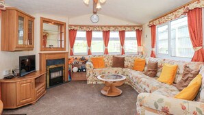 A cozy living room with a sofa, a television, a fireplace, and a clock on the wall. - Ty Newydd Caravan (Pwllheli)