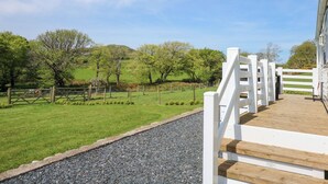 A wooden deck with white railings overlooking a grassy field and trees. - Ty Newydd Caravan (Pwllheli)