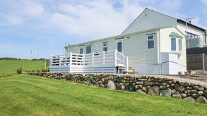 A two-story house with a stone wall in front, a white fence, and a grassy field. - Ty Newydd Caravan (Pwllheli)