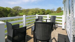 A balcony with wicker chairs and a white fence overlooking a green landscape. - Ty Newydd Caravan (Pwllheli)