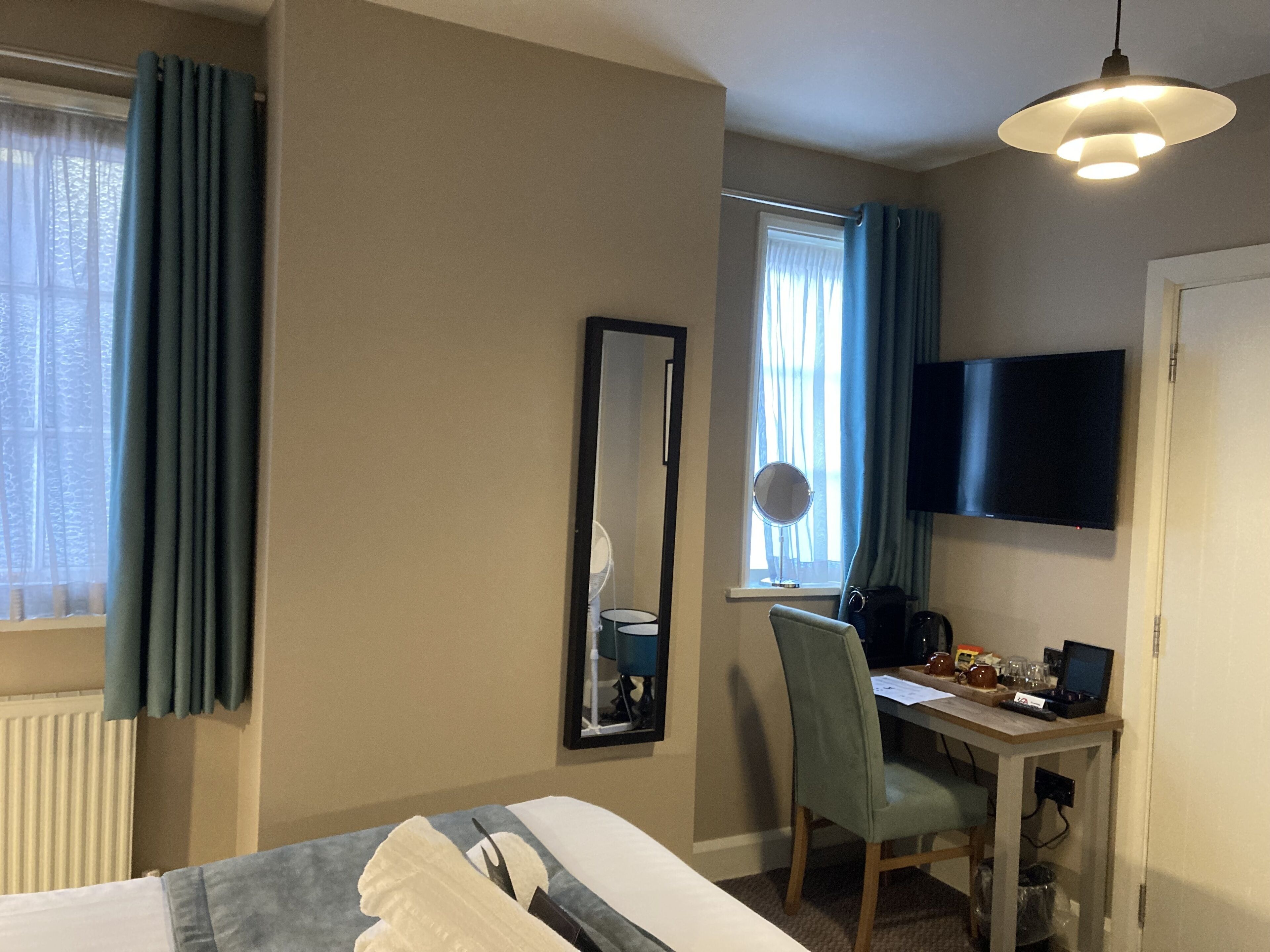 Une chambre d’hôtel comprenant un lit, un bureau avec une chaise, une télévision, un miroir et une fenêtre avec des rideaux.