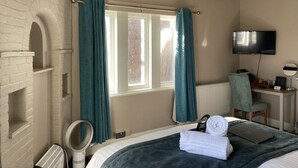 A hotel room with a bed, a desk with a computer, a TV, and a window with curtains. - Station Inn (Whitby)