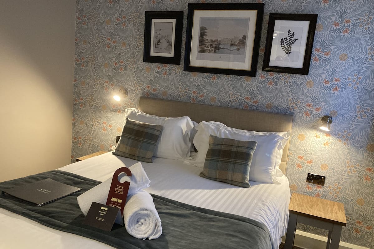A neatly made bed with a plaid blanket and pillows, a rolled towel, a laptop, and a sign indicating a quiet room.