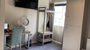 A bedroom with a bed, a desk with a chair, a TV, a wardrobe, and a window with curtains. - Station Inn (Whitby)
