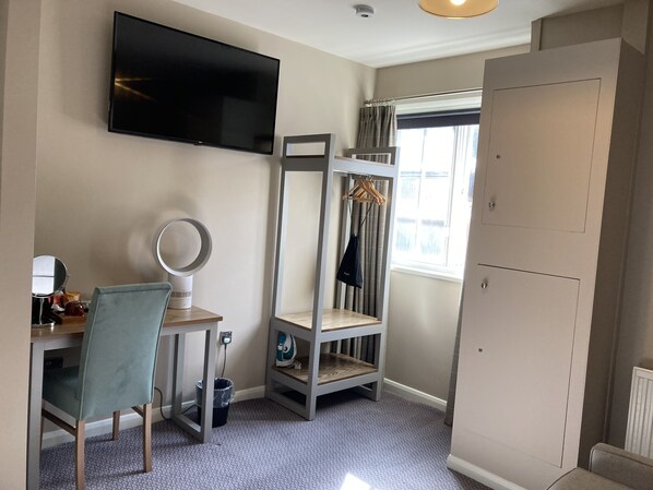 A bedroom with a bed, a desk with a chair, a TV, a wardrobe, and a window with curtains.