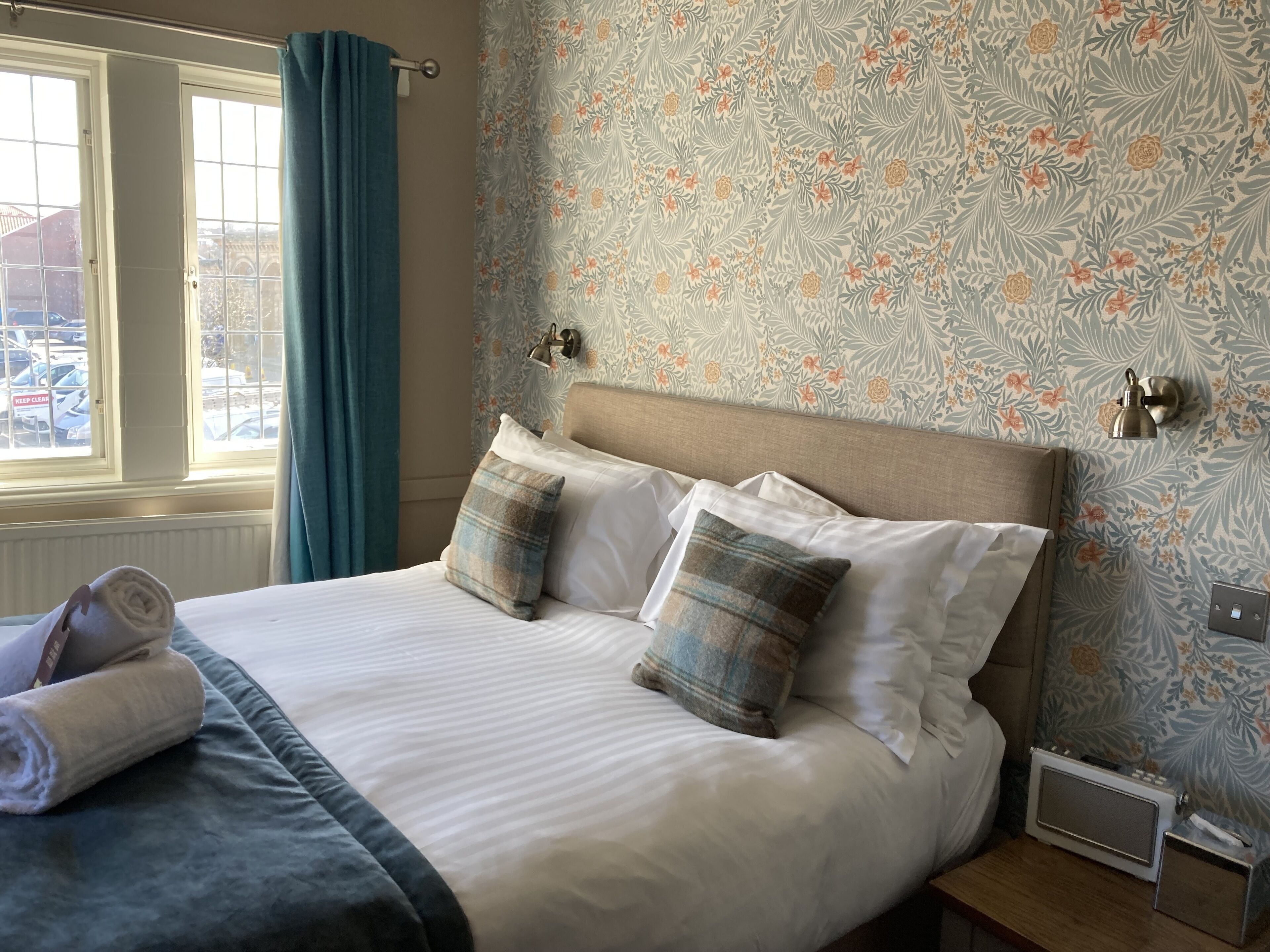 A neatly made bed with a headboard, two pillows, and a rolled towel on a dark-colored bedspread.