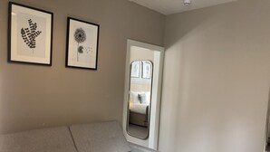 A neutral-toned room with a grey sofa, two framed botanical prints on the wall, and a mirror reflecting a bed with pillows. - Station Inn (Whitby)
