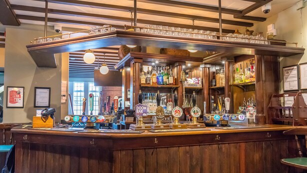A bar with wooden counter, multiple taps, and shelves with bottles. - Station Inn (Whitby)