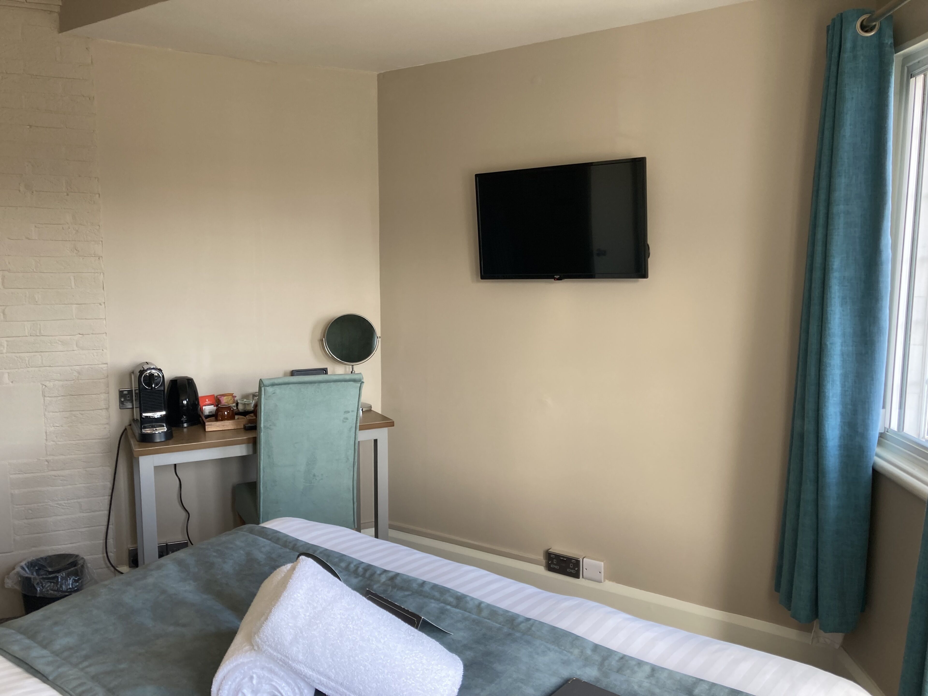 A hotel room with a bed, a desk with a coffee maker, a TV, and a window with curtains.