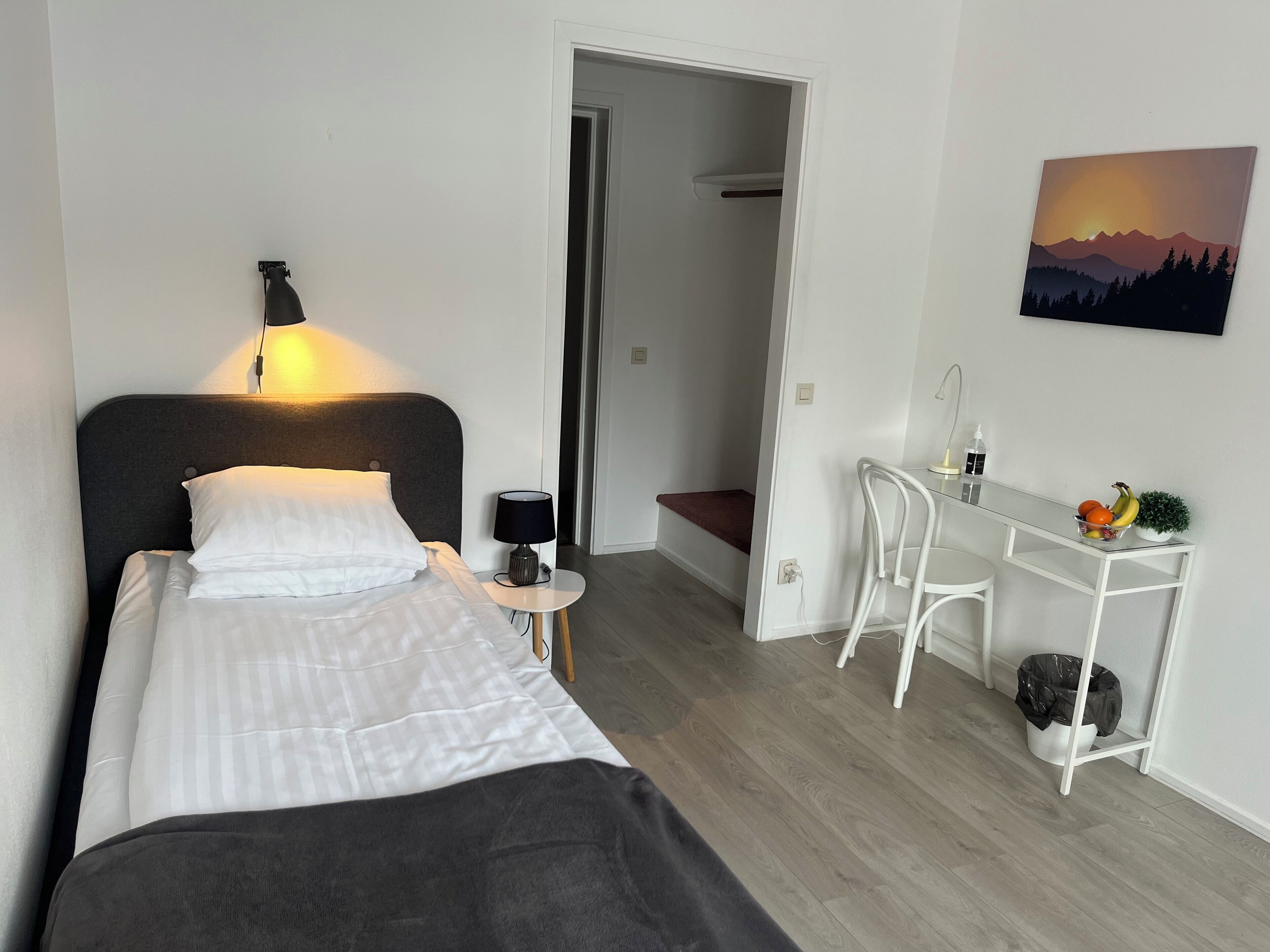 Una habitación de hotel moderna con cama, mesita de noche, lámpara y escritorio con silla.
