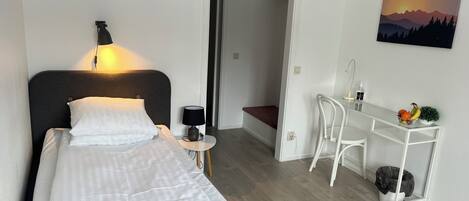 Una habitación de hotel moderna con cama, mesita de noche, lámpara y escritorio con silla.