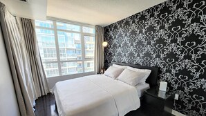 Ein Schlafzimmer mit einem großen Bett, einem Fenster mit Vorhängen und einer schwarz-weiß gemusterten Wand.