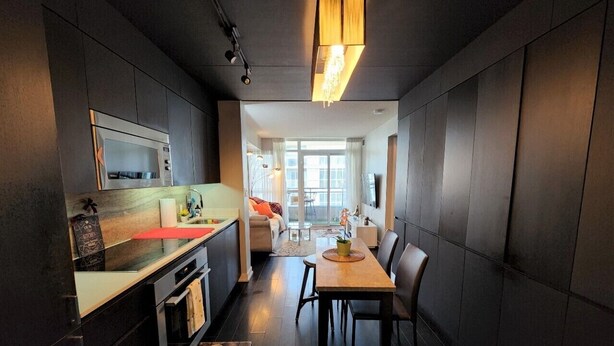Eine moderne Küche mit integriertem Backofen, ein Essbereich mit Holztisch und Stühlen sowie Blick in einen Wohnraum mit Sofa und Couchtisch.