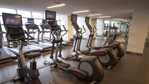 Ein Fitnessstudio mit Laufbändern, Crosstrainern und Ergometer, ausgestattet mit großen Fenstern und Spiegeln.