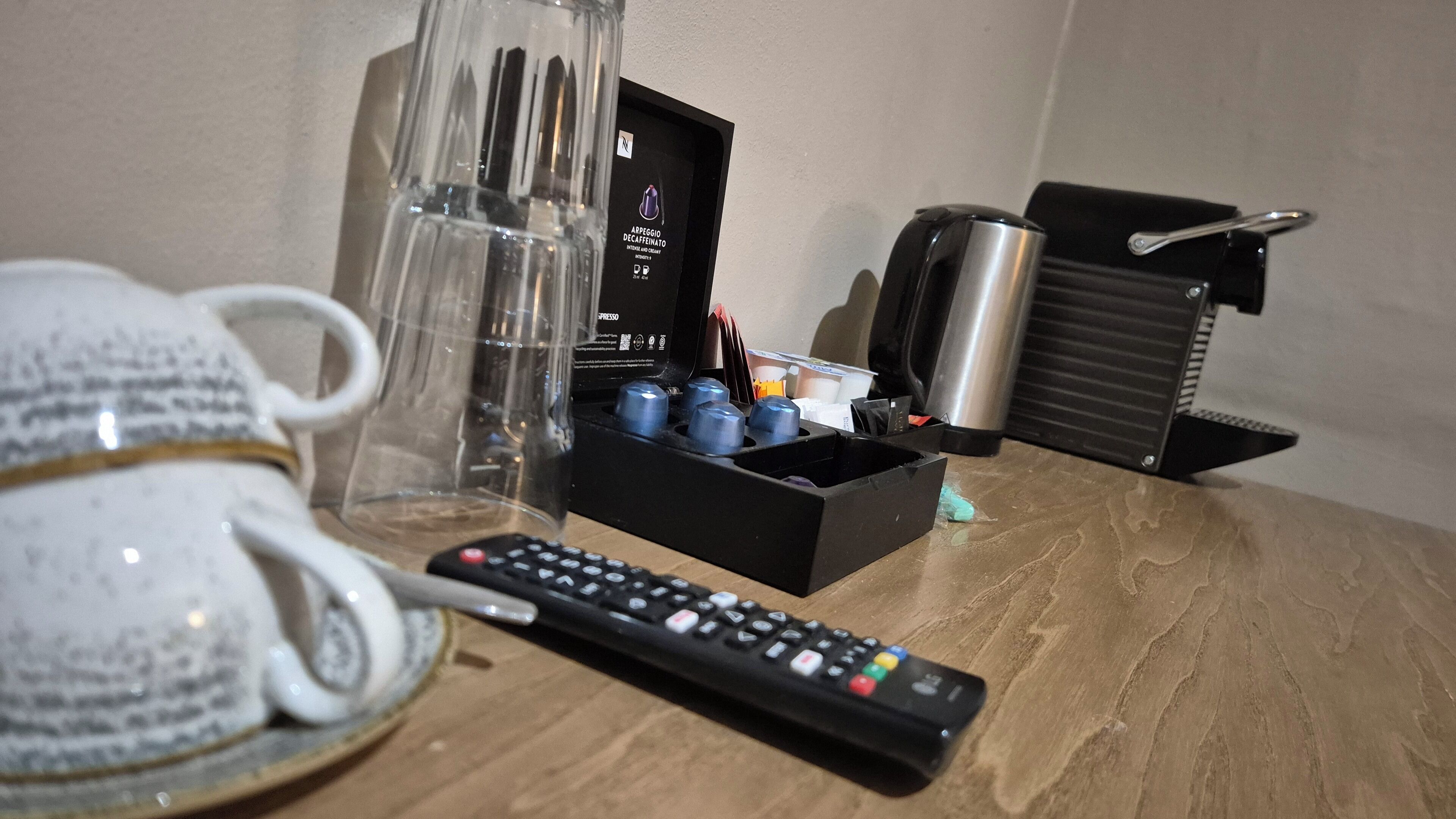 A coffee maker, a remote control, and a mug on a wooden table.