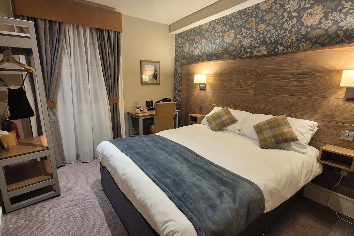 Ein Hotelzimmer mit Bett, Nachttischen, Schreibtisch, Kleiderschrank und Duschbereich.