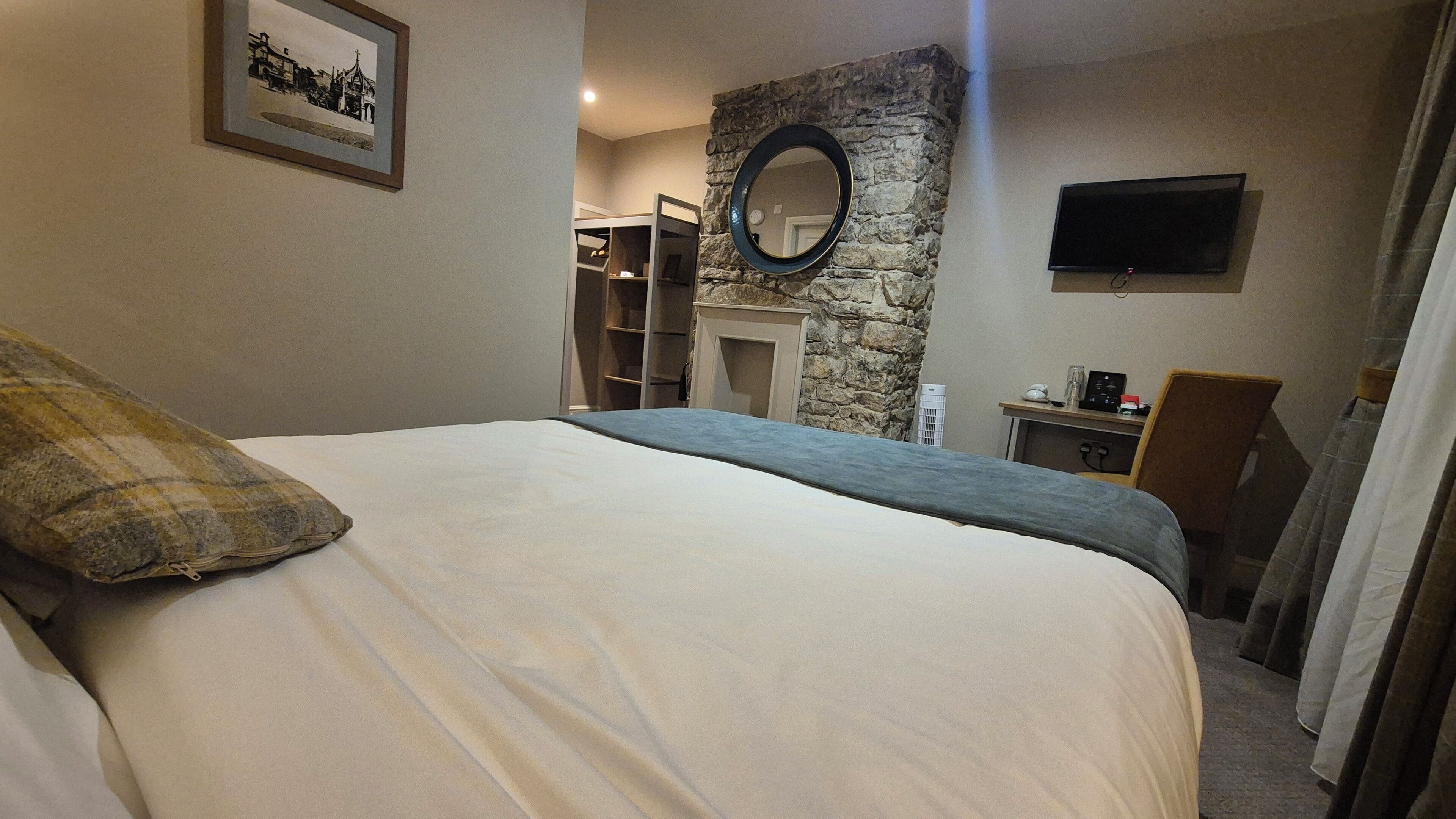 A bedroom with a bed, a stone wall, a fireplace, a television, and a wardrobe.