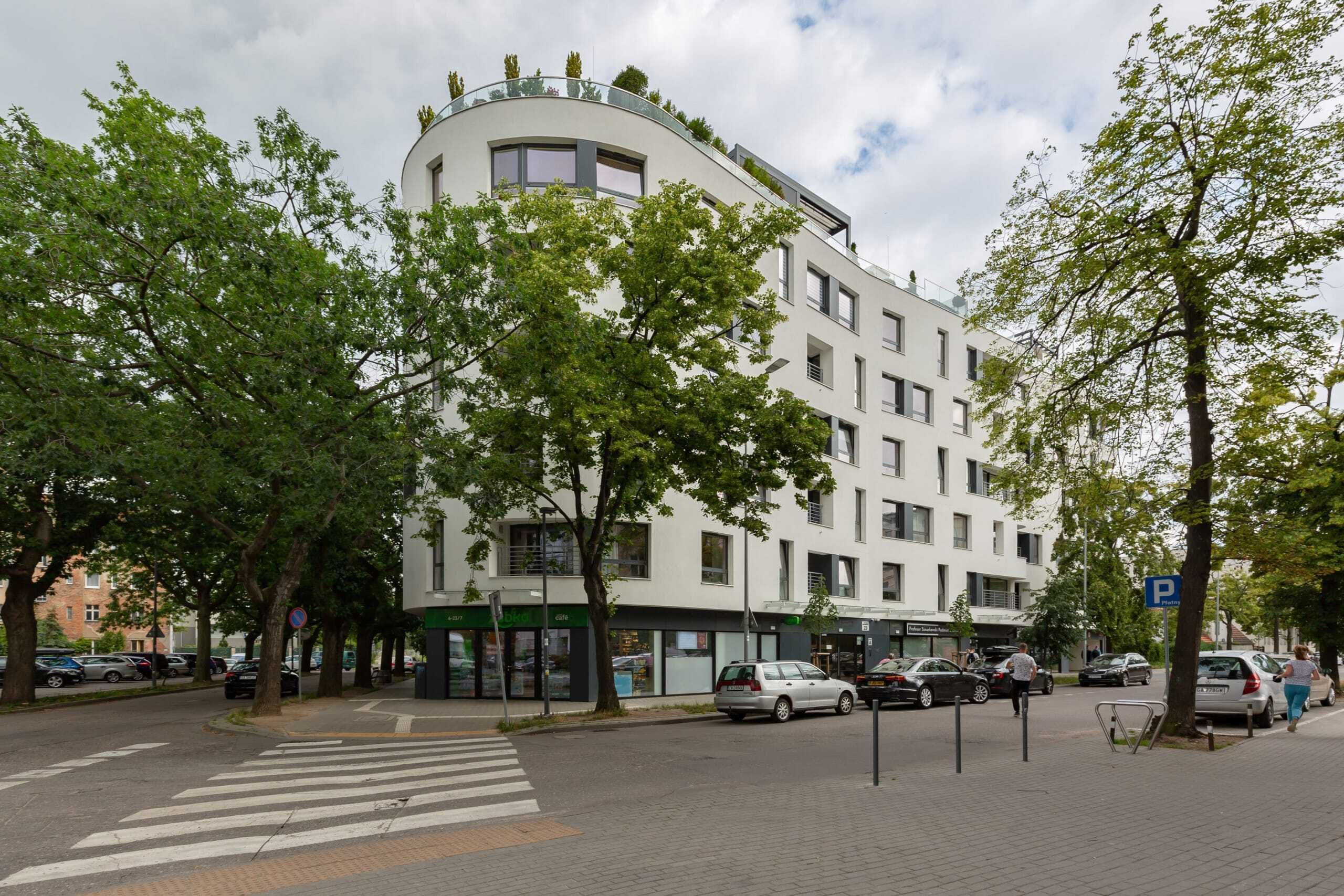 A modern building with a curved facade, multiple floors, and a flat roof with greenery.