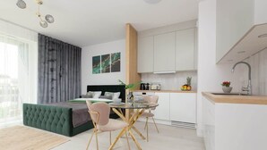 Een modern appartement met een groene bank, een glazen eettafel en een keuken met witte kasten.