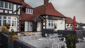 A traditional pub with a sign reading "THE OAK" and outdoor seating with metal chairs and tables. - The Oak (Coventry)