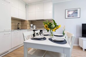 A modern kitchen with white cabinets, a coffee machine, and a dining table set for two with plates and cutlery.