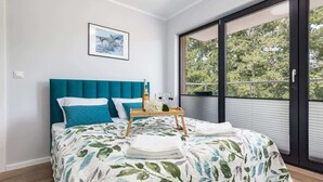 A bedroom with a bed, a window with a view of trees, and a framed picture on the wall. - Modern Apartment | 550 m to the Beach | Parking | Spa (Międzywodzie)