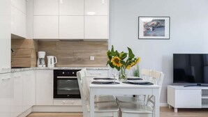 A modern kitchen with white cabinets, a built-in oven, and a dining area with a white table and chairs. - Modern Apartment | 550 m to the Beach | Parking | Spa (Międzywodzie)