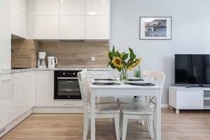 Une cuisine moderne avec des armoires blanches, un four encastré et un coin repas comprenant une table et des chaises blanches.