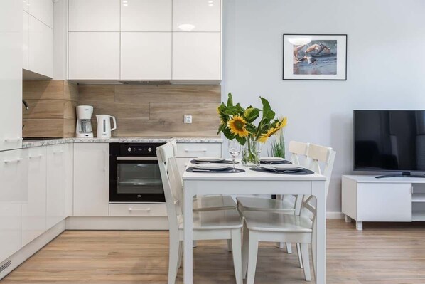 A modern kitchen with white cabinets, a built-in oven, and a dining area with a white table and chairs.